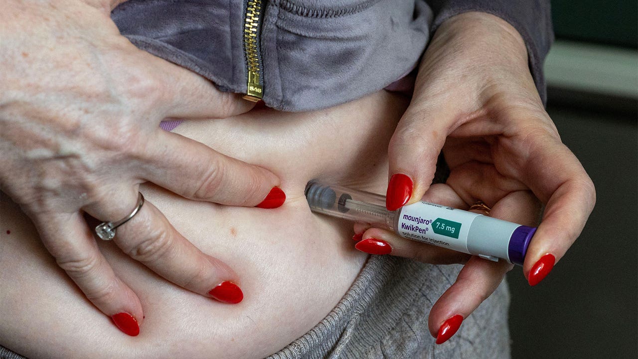 A photo of a woman self injecting her abdomen with a Mounjaro KwikPen.