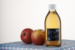 A bottle of apple cider vinegar next to apples on a table